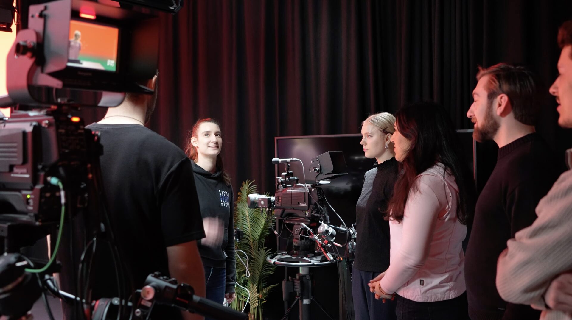 Mehrere Personen stehen zwischen Kamera- und Lichttechnik vor schwarzen Vorhängen und besprechen den Ablauf eines Drehs.
