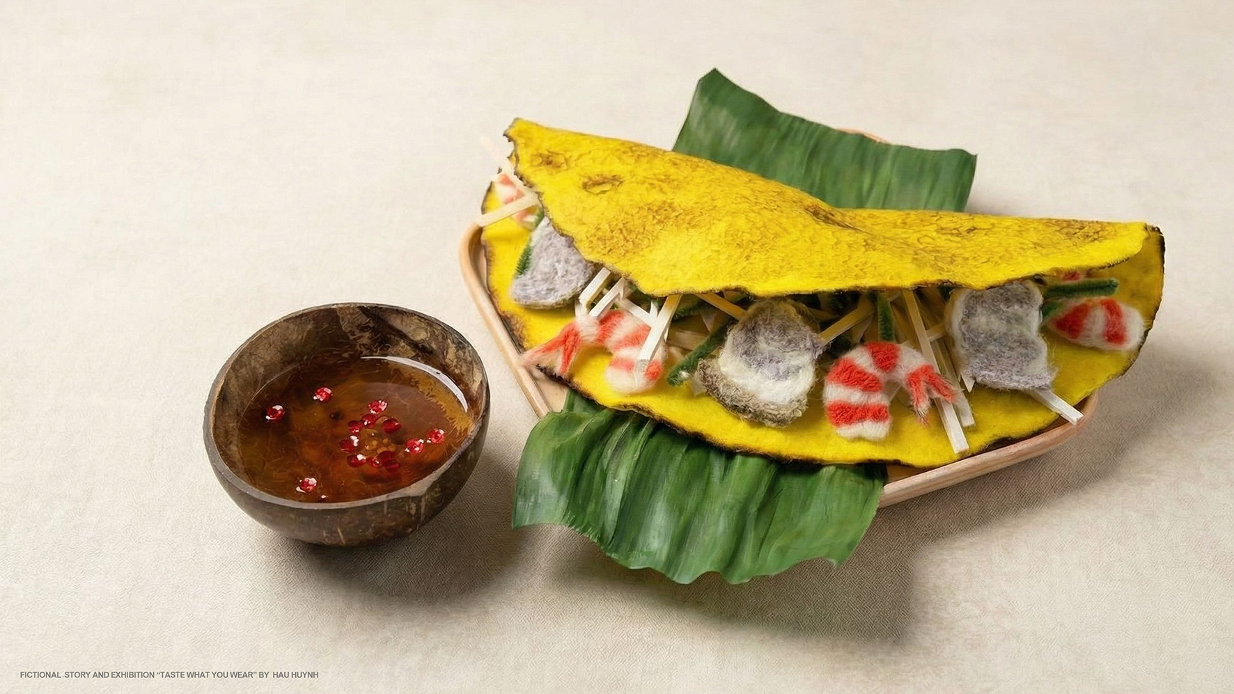 Stillleben: gefaltete gelbe „Taco“-Form aus Textil mit bunten, stoffartigen Füllungen; daneben eine Schale mit Sauce.